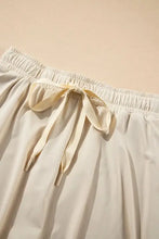 Cream-colored high-waisted shorts with pleated tennis skirt bow detail