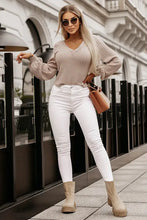 Beige lantern sleeve blouse with long sleeves, V-neck, and textured knit, paired with white jeans and tan boots
