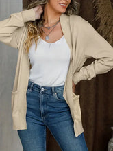 Frau in beigem Langarm-Strickjacke, weißem Top, blauer Jeans