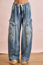 Light-wash denim baggy barrel jeans with cargo pockets and cream-colored drawstring waistband in relaxed wide-leg fit