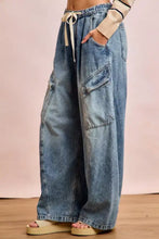 Wide-leg faded blue denim baggy barrel jeans with large cargo pockets and elastic waistband with cream drawstring