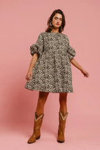 A woman wears a bi bi leopard denim dress with puffy sleeves and back contrast tie detail paired with tan boots