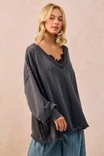 Dark gray oversized sweatshirt with v-neck and frayed hem made of french terry paired with white sneakers