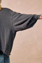 Dark gray oversized french terry sweatshirt with relaxed fit and frayed hem paired with white sneakers