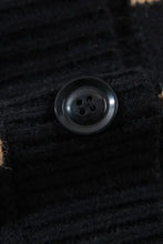 Black corduroy button with four holes and silver rim on cardigan sweater