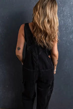 Woman in pocketed straight denim overalls with long wavy blonde hair