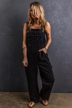 Woman in black pocketed straight denim overalls with wide legs and brown sandals