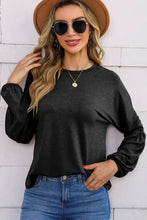 Woman in black round neck balloon sleeve top, jeans, hat, sunglasses