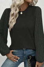 Schwarzes Langarmshirt mit rundem Ausschnitt, gerippten Ballonärmeln und hellblauen Jeans