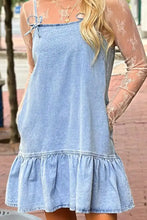 Light blue denim dress with adjustable spaghetti straps and a ruffle hem featuring a bow detail