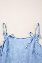 Light blue denim dress with ruffle hem and tied bow details on spaghetti straps at the shoulders