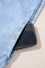 A sleek black smartphone rests in the seam of light-wash denim jeans beside a bow detail denim dress with ruffle hem and spaghetti straps