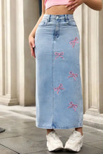 Light blue denim maxi skirt with pink embroidered bows along the side featuring a feminine bow-embroidered design