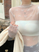 Sheer light pink mesh top featuring delicate white bow embroidery across the fabric for an elegant look