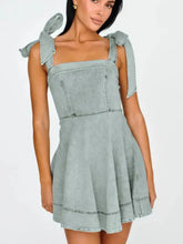A light blue denim mini dress with square neckline, tied shoulder bows, and slightly stretchy fabric