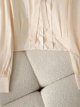 Cream-colored satin bow tie long sleeve shirt with button-front and ruffled detailing for elegant wear