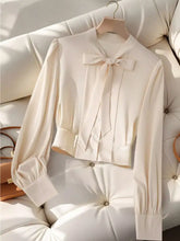 Cream-colored satin bow tie long sleeve shirt with prominent neckline bow and puffed sleeves