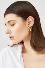 Woman wearing brass bow stud earrings with gold bow design