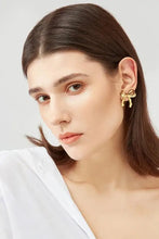 Woman in white shirt with brass bow stud earrings and golden bow ear cuff