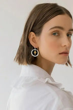 Woman in white shirt wearing brass contrast cross dangle earrings