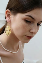 Woman in brass cutout leaf shape earrings with gold marquise earring
