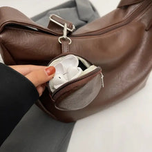 Brown leather crossbody bag with detachable circular mini pouch holding white earbuds