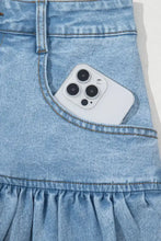 White iphone 12 pro with triple-camera system peeking out of a light-wash bubble hem denim mini skirt pocket