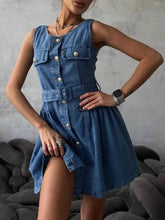 Blue sleeveless denim dress with front button closure, two chest pockets, and belted waist in denim material