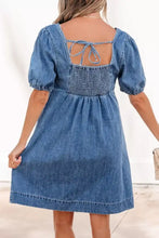 Back view of a blue button-front puff sleeve denim dress with square back and fabric ties in puff sleeve denim style
