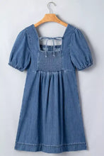 Button-front puff sleeve denim dress featuring a square neckline and smocked front detailing in blue denim fabric