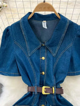 Blue denim dress with collar, short puffed sleeves, gold buttons, and brown belt with yellow buckle in short sleeve denim style