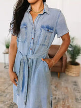 Light blue short sleeve denim dress with button front chest pockets and tied waistband in denim fabric