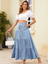 A light blue tiered denim dress with ruffled maxi skirt and front button closure made of denim material