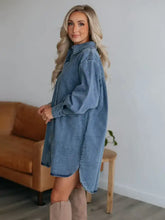 A long light-wash denim dress with a collared neck long sleeve and button-front design