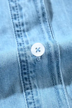 A white round button with a cross-shaped hole on light blue denim fabric of a notched long sleeve denim dress