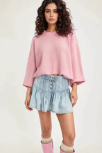 A soft pink ribbed knit cropped sweater with bell sleeves paired with a buttoned ruffled mini denim skirt