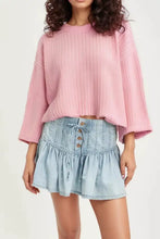 Pink ribbed knit cropped sweater with bell sleeves paired with a buttoned ruffled mini denim skirt in blue denim