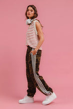 A woman wearing BiBi side lines camouflage track pants with three white stripes and a red and white knit sleeveless top