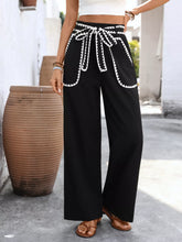 Black wide leg trousers with white crochet trim tie waist and embroidered trim along waistband and pockets