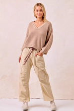 Beige ribbed knit v-neck sweater with long sleeves and drawstring waist paired with drawstring striped twill barrel pants