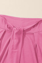 Pink pleated skirt with gathered waistband styled as knotted waist split leg relaxed pants for casual wear