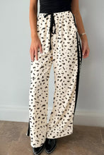 Cream-colored loose drawstring pants with leopard print black abstract dots and contrasting black side stripes