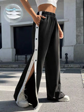 Black two-tone snap wide leg pants featuring a white vertical stripe and button details down the side