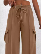 Tan cargo pants with elastic waistband and drawstring featuring large side pockets in casual high waist style
