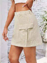 Beige cargo denim skirt with front flap pocket secured by metal ring and drawstring casual cargo denim skirt