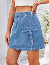 A mid-thigh length medium blue wash cargo denim skirt with elastic waistband and large cargo pockets with metal rings