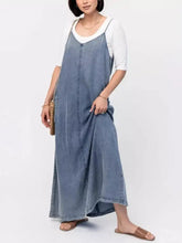 A casual washed denim maxi dress in light-wash with adjustable straps worn over a white top