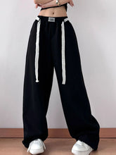 Black elastic waist wide leg pants with white beaded drawstrings and a silver rectangular belt buckle