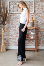 Heimish full size black wide-leg solid damask casual pants with intricate white embroidered detailing at the cuffs