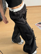 Black cargo pants with white bow elastic waist and multiple side pockets secured by fabric ties elastic waist cargo design